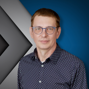 Porträt eines Mannes mit kurzen braunen Haaren, Brille und gemustertem Hemd. Er steht vor einem blauen und grauen Hintergrund mit grafischen Pfeilen.